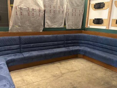 Blue sectional sofa in showroom with protective plastic covers and wrapped chairs displayed on shelves above