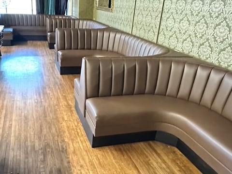 Modern restaurant booth seating with tan leather banquettes and striped back panels along a wooden floor