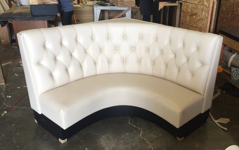White curved tufted sofa with black base in furniture showroom or warehouse setting