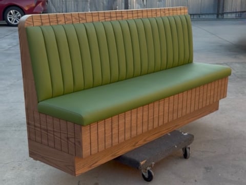 Green and tan vinyl booth seating with vertical stitching on wooden base with casters