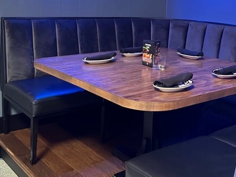 Modern dining booth with blue upholstered seating, wooden table with place settings, blue accent lighting, and contemporary interior design