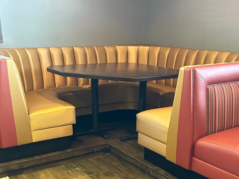 Retro diner booth with yellow and red vinyl seating and a black oval table