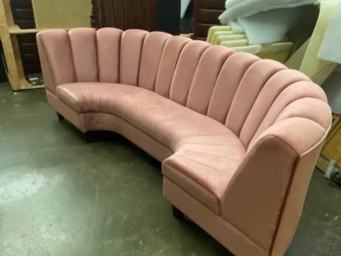 Pink curved sectional sofa with vertical channel tufting on concrete floor in showroom