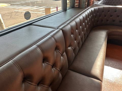 Brown leather tufted booth seating along a large window in a modern interior space