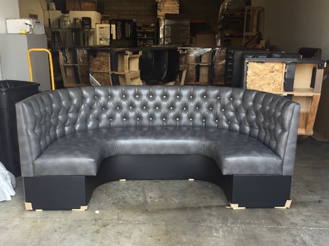 Gray tufted leather curved banquette seating in warehouse with stacked furniture in background