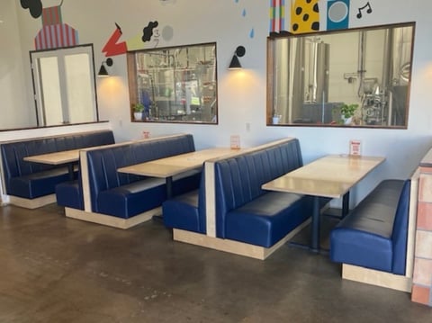 Modern cafe dining area with blue booth seating, wooden tables, pendant lights, and colorful wall art on polished concrete floor