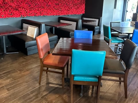Modern office break room with wooden table, colorful chairs in turquoise and coral, and seating areas with red acoustic panels on walls
