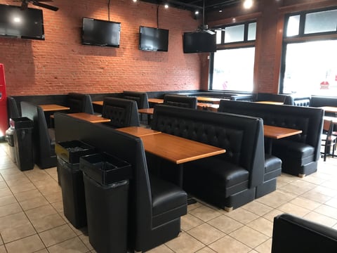 Modern restaurant interior with black booths and wood-top tables, exposed brick walls, and wall-mounted TVs